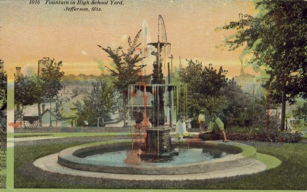 Colorized postcard view of children sitting around a fountain. Caption reads: "Fountain in High School Yard, Jefferson, Wis."