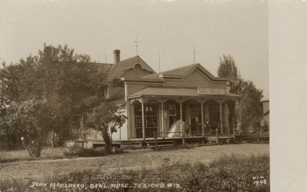 Photographic postcard view of a general store. There is a group of people gathered on the porch. Caption reads: "John Mahlberg, General MDSE, Jericho, Wis."