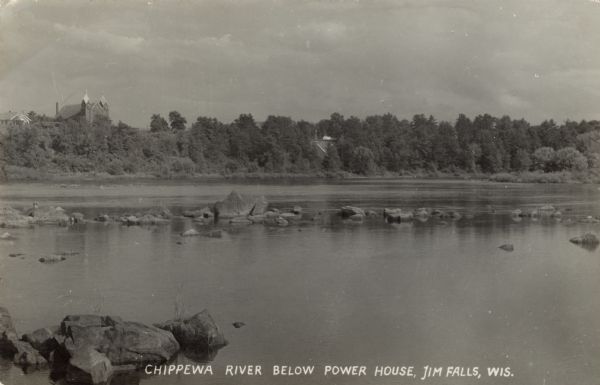 View from shoreline across the Chippewa River. There is a church on the opposite shoreline behind trees. Caption reads: "Chippewa River below power house, Jim Falls, Wis."