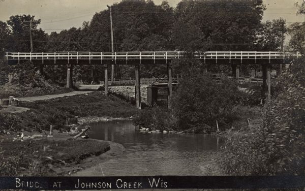 View of two bridges crossing Johnson Creek, a higher bridge and a lower one. A road along the creek. Caption reads: "Bridges at Johnson Creek, Wis."