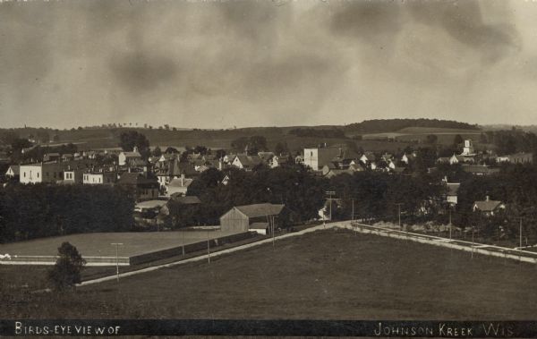 Photographic postcard view of the rooftops of Johnson Creek and surrounding landscape. Caption reads: "Bird's-Eye View of Johnson Kreek[sic] Wis."