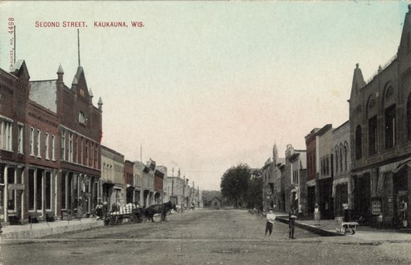 View of the businesses lining Second Street. There is a horse and wagon at the curb, and boys are standing in the street. Caption reads: "Second Street, Kaukauna, Wis."