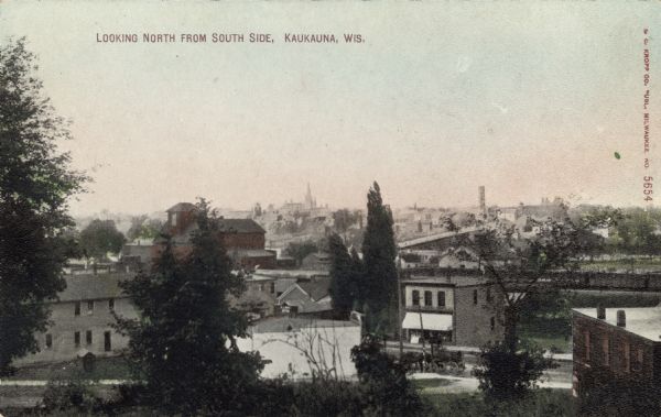 Elevated view of Kaukauna's south side, with the north side in the distance. There is a bridge over the Fox River. Caption reads: "Looking North from South Side, Kaukauna, Wis."