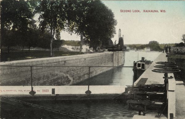 View of a lock on the Fox River. There is a boat in the canal, and pedestrians standing on the canal wall on the right. Caption reads: "Second Lock, Kaukauna, Wis."