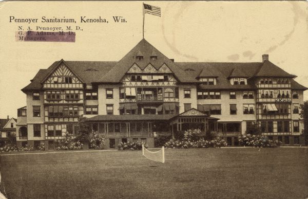 View across lawn toward the sanitarium. There is a net set up on the lawn in the foreground. Caption reads: "Pennoyer Sanitarium, Kenosha, Wis. N.A. Pennoyer, M.D., G.F. Adams, M.D., Managers."