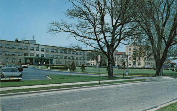 Ektochrome postcard of St. Catherine's Hospital and entry drive. Automobiles are parked in the lot.