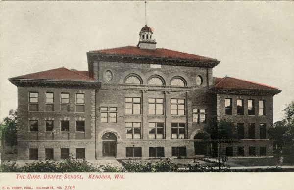 Color illustration of a school building. Oval and arched windows are above the arched entrances. Caption reads: "The Chas. Durkee School, Kenosha, Wis."