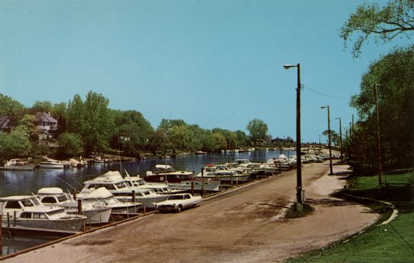 View of a marina in a canal. One row of boats is moored along a road.