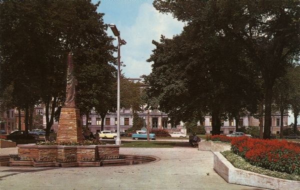 Ektachrome postcard of the park across from the courthouse. The Boy Scouts Monument (a replica of the Statue of Liberty) is in the center surrounded by flower beds.