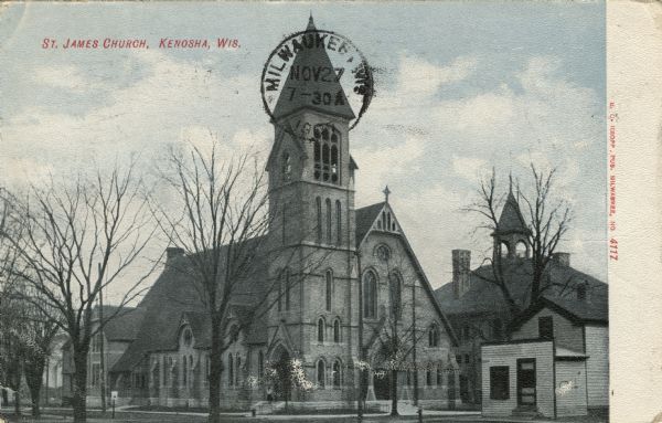 Photographic postcard view across street towards a church with a steeple at the corner of an intersection. Caption reads: "St. James Church, Kenosha, Wis."