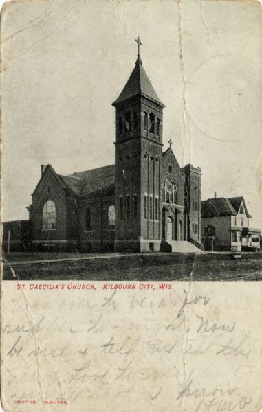 Corner view of St. Caecilia's Church. Romanesque arches are on the windows and steeple. A dwelling (perhaps a parsonage) is next door.Caption reads: "St. Caecilia's Church, Kilbourn City, Wis."