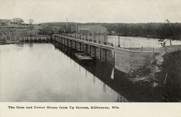 Slightly elevated view of the dam and power house from across the Wisconsin River. Caption reads: "Dam and Power House from Up Stream, Kilbourne [sic], Wis."