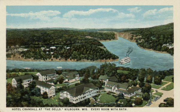 Aerial view of a hotel with multiple buildings near a bend in the Wisconsin River. A paddle-wheel steamer is heading toward the Dells. Caption reads: "Hotel Crandall at 'The Dells.' Kilbourn, Wis. Every Room With Bath."