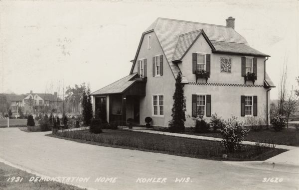 A two-story stone home in a Germanic-Austrian style. A decorative tile is set into the exterior between the windows on the second floor. Caption reads: "1931 Demonstration Home, Kohler, Wis."