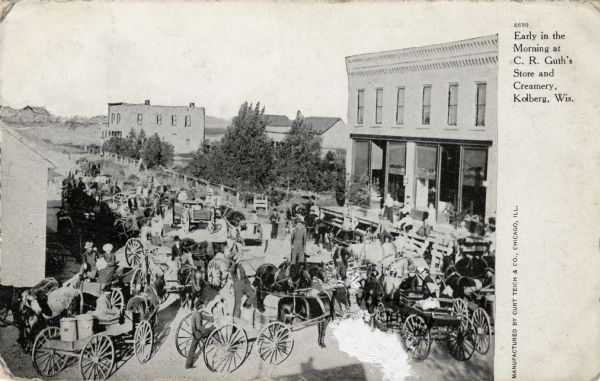 Elevated view of a gathering of people with horses and wagons delivering goods to a general store. Caption reads: "Early in the Morning at C.R. Guth's Store and Creamery, Kolberg, Wis."
