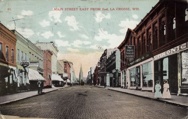 Colorized view looking down Main Street. Businesses include a printer, a furniture store, and a telegraph office. A church is on the horizon. Two women are standing on the sidewalk on the right. Caption reads: "Main Street East from 2nd, La Crosse, Wis."