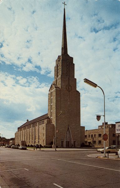 Corner view of St. Joseph's Cathedral, dedicated 1962. There is a clock in the steeple face. Automobiles are parked along the curbs.
