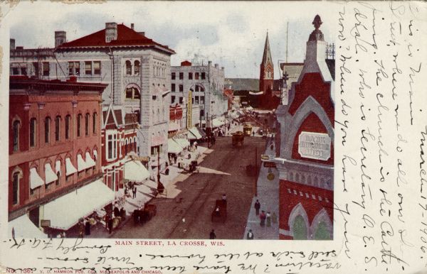Hand-colored, elevated view of Main Street, with a bank in the foreground on the right, and a church in the distance. Caption reads: "Main Street, La Crosse, Wis."