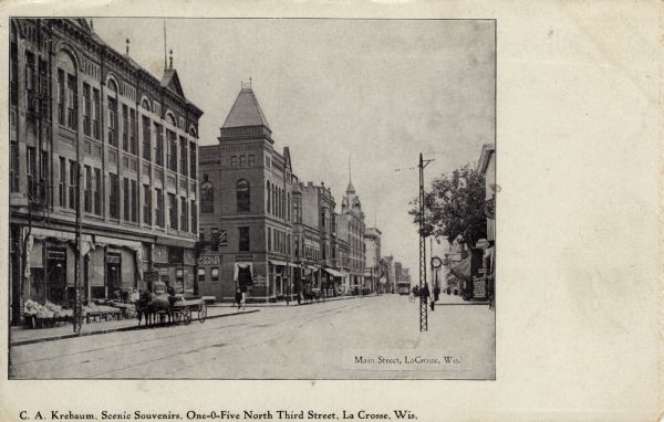 View across street towards left side of Main Street. There are two dentist offices on the left, and two clocks are on the right. Horses and carts are along the curb. Caption reads: "Main Street, La Crosse, Wis."