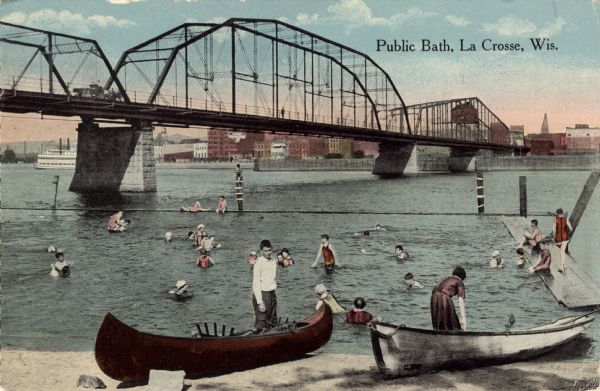 A bathing beach on an island near a bridge, with people in the water and on the beach within an enclosed area. A canoe and rowboat are pulled up on the shore in the foreground. The La Crosse skyline is in the background. A horse and cart, and pedestrians are crossing the bridge. Caption reads: "Public Bath, La Crosse, Wis."