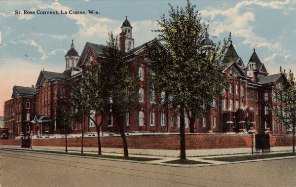 View across intersection towards a large convent. There is a brick wall  along the sidewalk surrounding the convent. Caption reads: "St. Rose Convent, La Crosse, Wis."