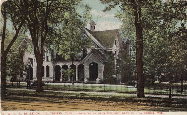 View across street towards the YWCA Building, with a lawn and fence surrounding the grounds. Caption reads: "Y. W. C. A. Building, La Crosse, Wis."