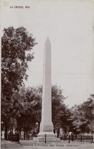 View of the Washburn Monument obelisk surrounded by a fence in Oak Grove Cemetery. Caption at the top reads: "La Crosse, Wis." Caption at the bottom reads: "Washburn Monument Oak Grove Cemetery."