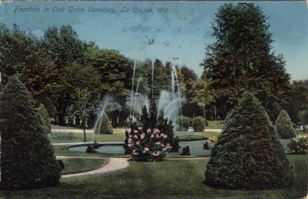 Hand-colored view of a fountain obscured by a flowering bush. Caption reads: "Fountain in Oak Grove Cemetery, La Crosse, Wis."