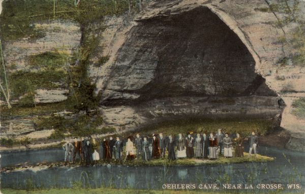 Hand-colored view of the entrance to Oehler's Cave. A group of people are gathered on an island in the stream at the mouth of the cave. Caption reads: "Oehler's Cave,  near La Crosse, Wis."
