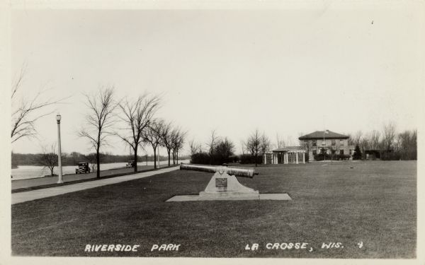 View of the cannon at Riverside Park. Automobiles are parked by the river on the left. Caption reads: "Riverside Park, La Crosse, Wis."