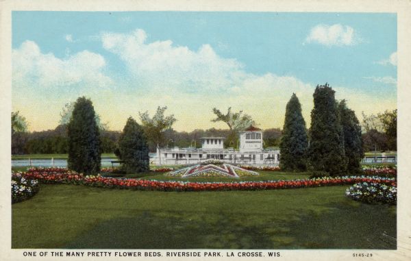 View of flower beds in a park. An excursion boat is in the Mississippi River in the background. Caption reads: "One of the Many Pretty Flower Beds, Riverside Park, La Crosse, Wis."