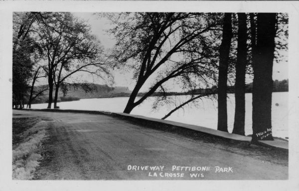 View of a driveway and sidewalk along the Mississippi River. An interstate bridge and bluffs are in the distance. Caption reads: "Driveway, Pettibone Park, La Crosse, Wis."