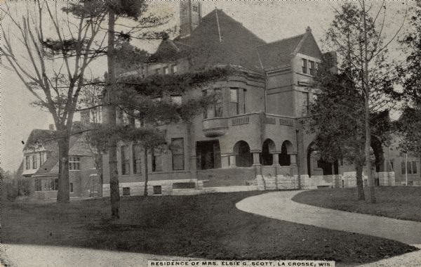 View across lawn towards a large home. The curved driveway the leads to a series of arches at the porte cochère entrance. Caption reads: "Residence of Mrs. Elsie G. Scott, La Crosse, Wis."