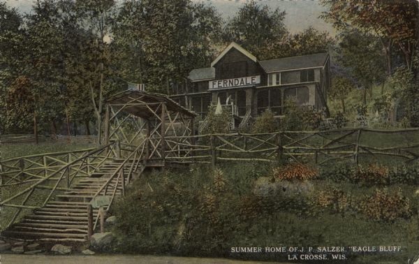 View uphill towards a summer home with a large screened-in porch and stairs leading up to the entrance. Halfway up the stairs is a roofed area over benches. A sign above the entrance reads: "Ferndale." Caption reads: "Summer Home of J.P. Salzer. 'Eagle Bluff,' La Crosse, Wis."