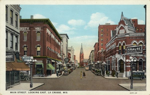 View toward Main Street intersection. The business school is on the left; Krause Clothing store is on the right. A church is at the end of the street. Automobiles are parked at the curbs, and streetcar tracks are running up the street. Caption reads: "Main Street, Looking East, La Crosse, Wis."
