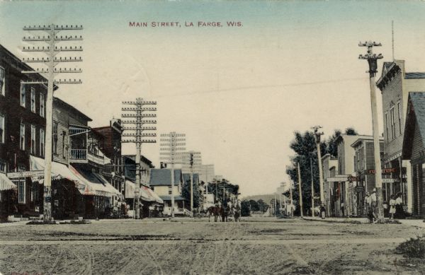 Hand-colored view of Main Street lined with businesses. Shoe stores are on both sides of the street. A team of horses is approaching. Caption reads: "Main Street, La Farge, Wis."
