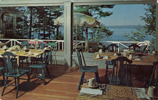 Color postcard view of the dining room, with large picture windows, and sundeck, with a view of Lake Superior and the mainland hills in the distance.