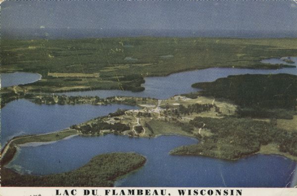 Kodachrome postcard of an aerial view of Lac du Flambeau village and the surrounding chain of lakes. Caption reads: "Lac du Flambeau, Wisconsin." Text on back reads: "The Village of Lac du Flambeau situated in the heart of the Chippewa Indian reservation."