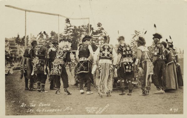 A group of Ojibwa dancers in a circle. Caption reads: "'At the Dance' Lac du Flambeau, Wis."