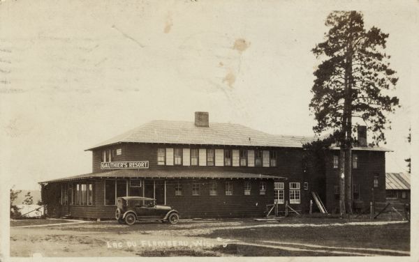 A wooden building with an automobile parked on the side. Caption reads: "Lac du Flambeau, Wis."