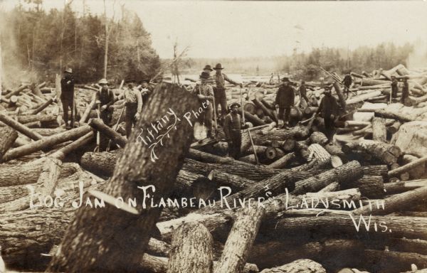 View of a group of men posing on a log jam in a river. Caption reads: "Log Jam on Flambeau River near Ladysmith, Wis."