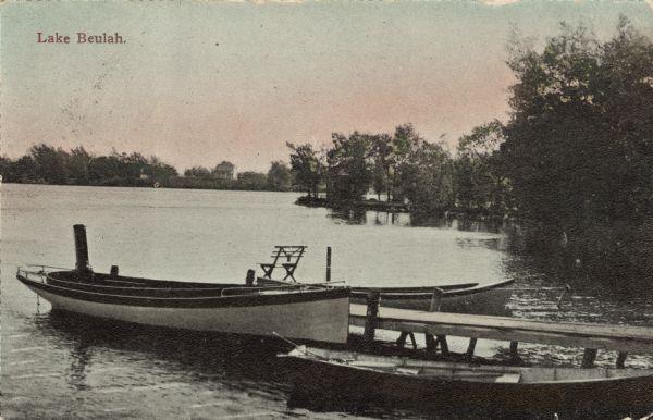 Rowboats docked near a small pier on a lake. A house is on the far shoreline. Caption reads: "Lake Beulah."