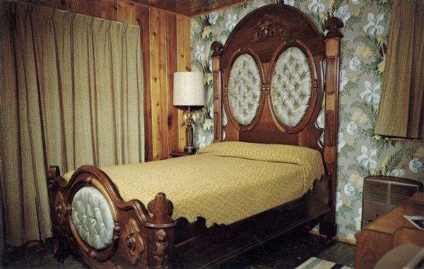 Interior of bedroom suite. Text on reverse reads: "This bed, vintage 1860, was obtained from an old home near Springfield, Ill. The rich black walnut was completely restored, buried panels were replaced with more decorative tufting, and for comfort a new box spring and mattress added. To claim that Abraham Lincoln actually slept in this bed would be presumptuous, but he could have."