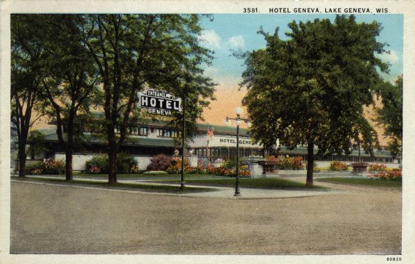 Hand-colored view from street towards the entrance of Hotel Geneva. There is a circular drive, and flowers and bushes planted at the front entrance. A large electric sign is at the corner. Caption reads: "Hotel Geneva, Lake Geneva, Wis."