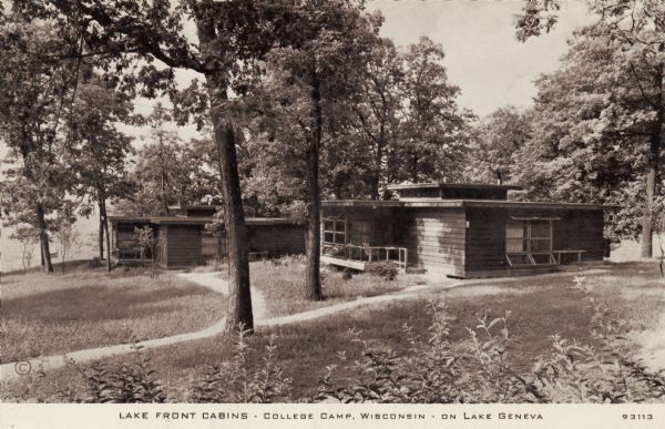 View of two cabins near the lake, which is in the background below the hill. The cabins have flat roofs and wood siding. Caption reads: "Lake Front Cabins &#8212; College Camp, Wisconsin &#8212; on Lake Geneva."