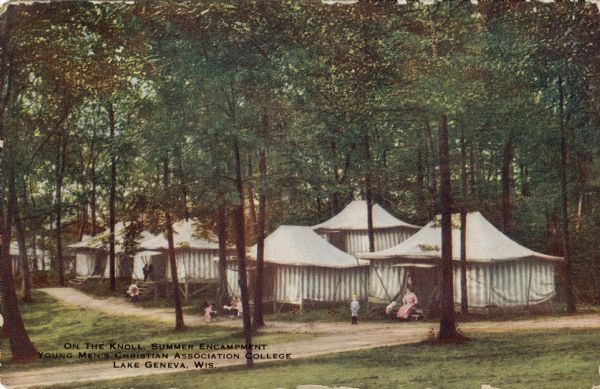 View of tents along a dirt road at the YMCA College summer camp. Each tent is raised up on platforms, with steps up to the entrance. A woman and children are sitting and standing outside a number of the tents. Caption reads: "On the Knoll, Summer Encampment, Young Men's Christian Association College, Lake Geneva, Wis."