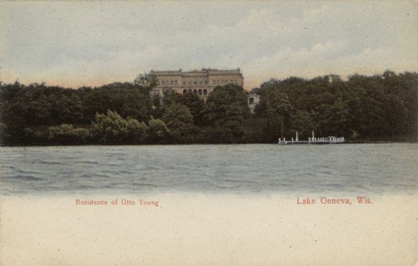 View across lake towards a large private home on Lake Geneva. There are arches and columns on the second floor. Caption reads: "Residence of Otto Young, Lake Geneva, Wis."