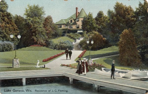 View from water towards a large private home on a hill on Lake Geneva. People are walking on a large pier at the water's edge, and rowboats are moored at the shoreline. Lampposts are along the walkways. Caption reads: "Lake Geneva, Wis. Residence of J.C. Fleming."