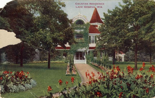 View across front lawn with curving sidewalk towards an ivy-covered house. There are flower beds along the walkway. Caption reads: "Countiss Residence, Lake Geneva, Wis."