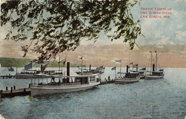 View from shoreline towards yachts moored at two long docks. Caption reads: "Private Yachts, at Lake Geneva Docks, Lake Geneva, Wis."